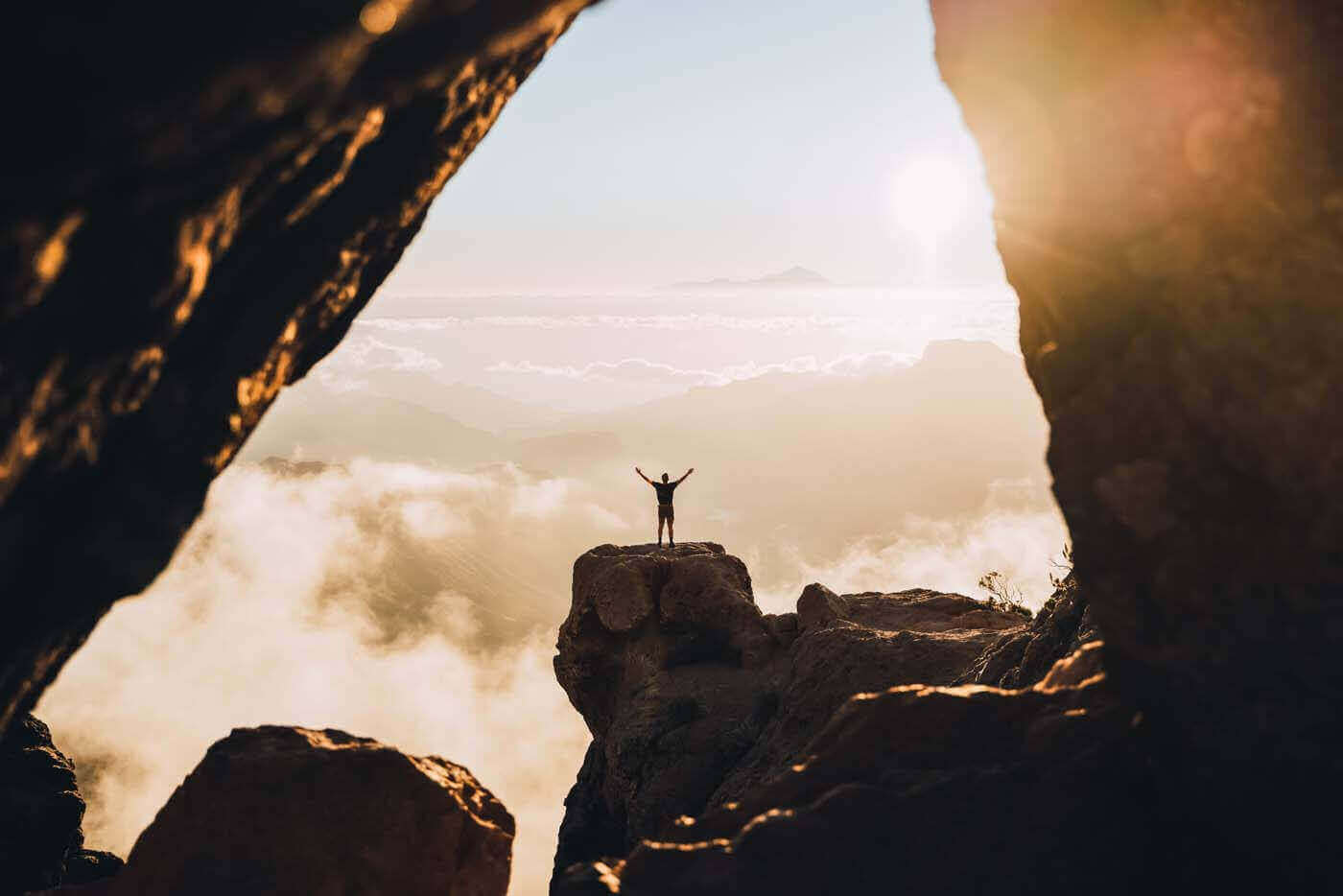 Man At The Top Of A Cliff During The Sunset With Raised Hands